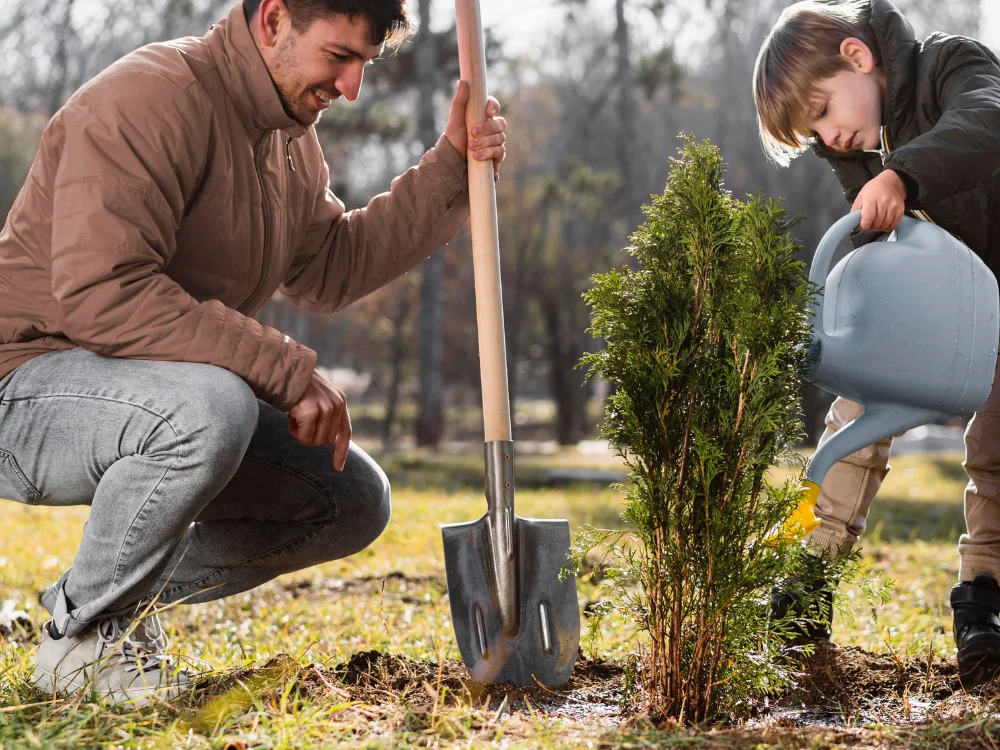 Un adulte et un enfant participent à la plantation et à l’arrosage d’un jeune arbre dans le cadre d’un projet environnemental.